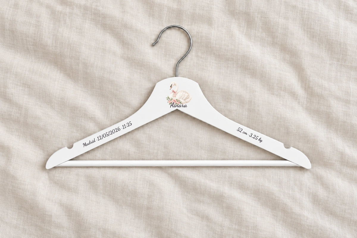 Percha bebé blanca personalizada con cisne, nombre Ainara y datos de nacimiento sobre lino claro