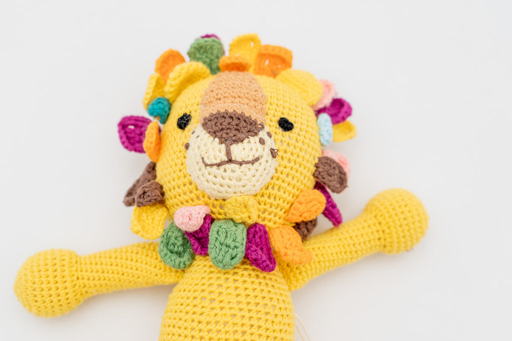 Plano medio de un león de crochet con brazos extendidos y melena multicolor.