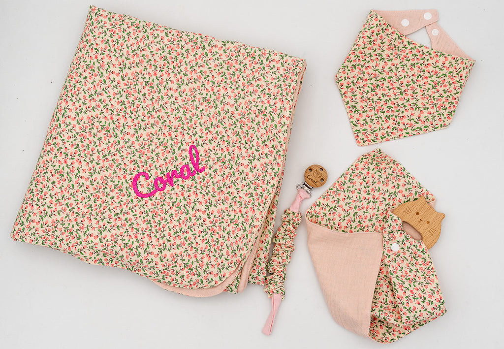 Ensemble rose avec couverture fleurie brodée du prénom Coral, bavoir bandana, lange rose avec anneau de dentition en bois et attache-tétine.
