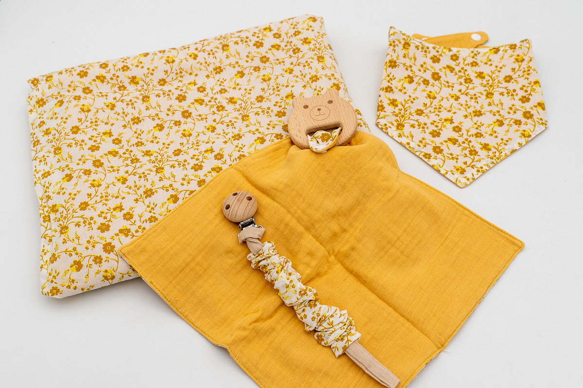 Ensemble moutarde avec couverture fleurie, bavoir bandana, lange moutarde avec anneau de dentition ourson en bois et attache-tétine à pince en bois.