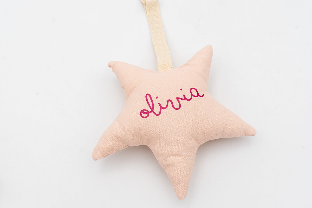 Estrella de tela rosa con el nombre olivia en el frontal y cinta para colgar