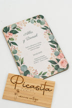 Faire-part de mariage en bois avec des feuilles d'eucalyptus et des roses dans les coins