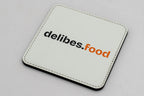 Sous-verre carré blanc avec logo delibes.Food noir et orange.