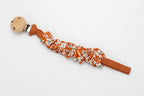 Attache-tétine en tissu froncé à fleurs sur fond terracotta avec clip en bois