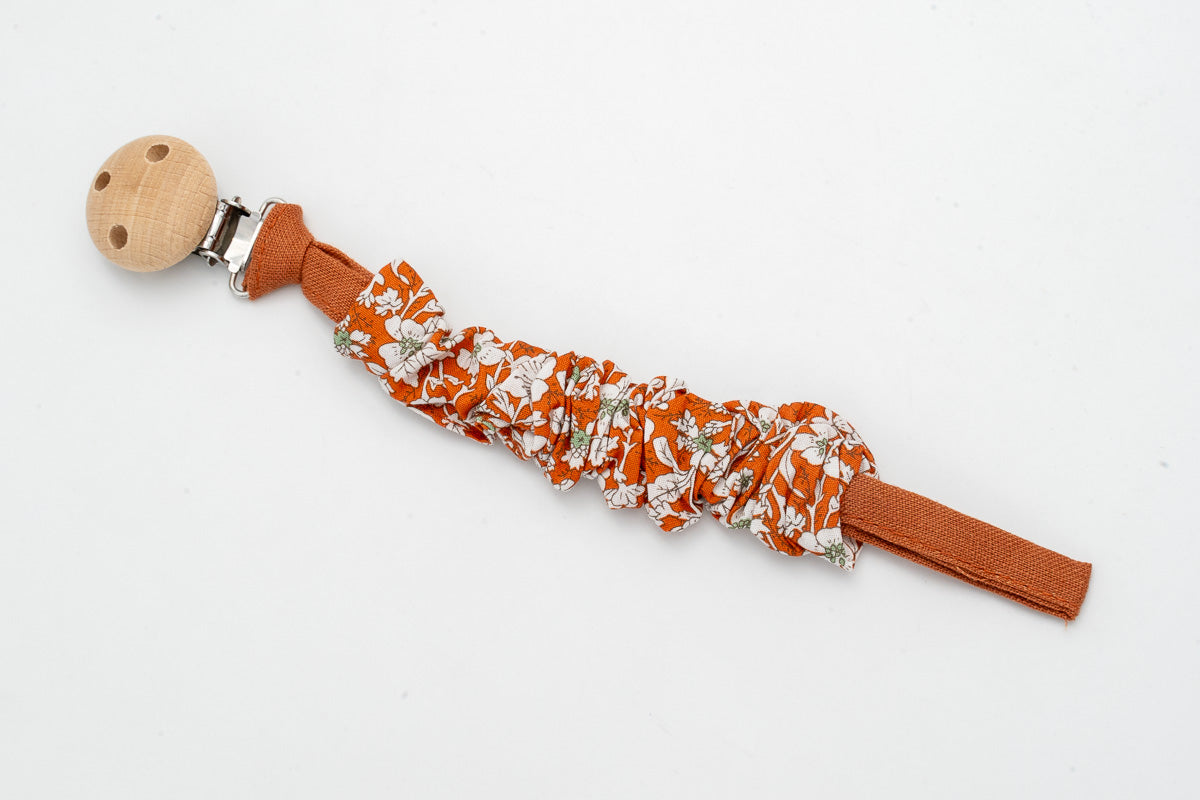 Attache-tétine en tissu froncé à fleurs sur fond terracotta avec clip en bois