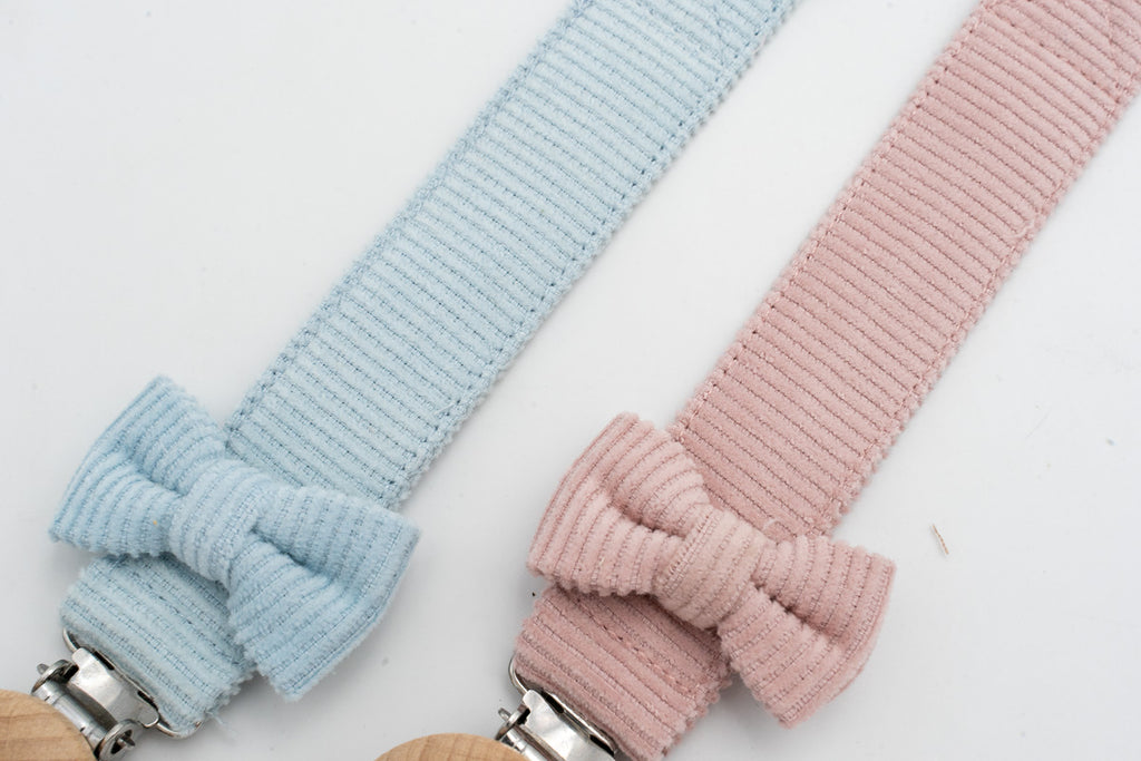 Détail des attaches-tétines à nœuds bleu clair et rose près de leurs clips en bois