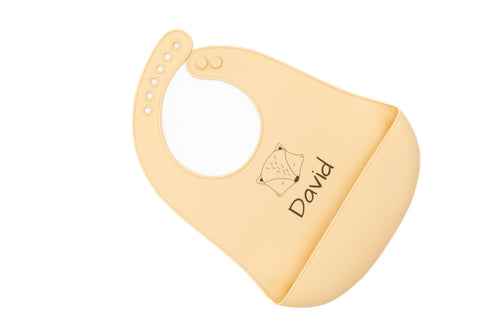 Bavoir en silicone beige avec prénom et motif animal géométrique, vu en diagonale.