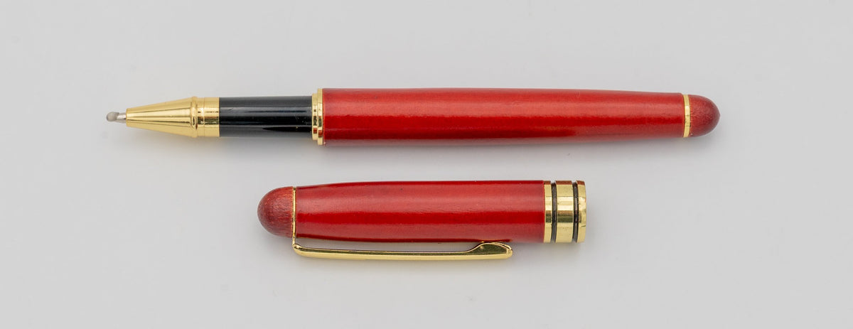 Stylo en bois de finition rougeâtre avec capuchon retiré et détails dorés.