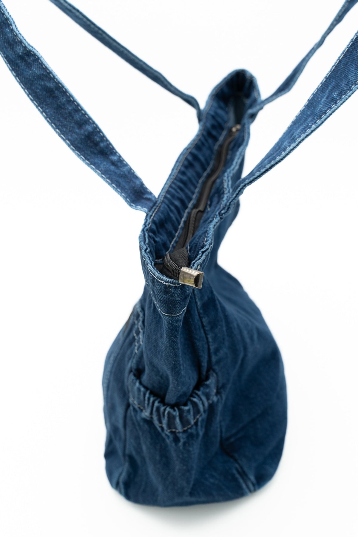Profil du sac en jean montrant la fermeture éclair supérieure et une poche latérale froncée