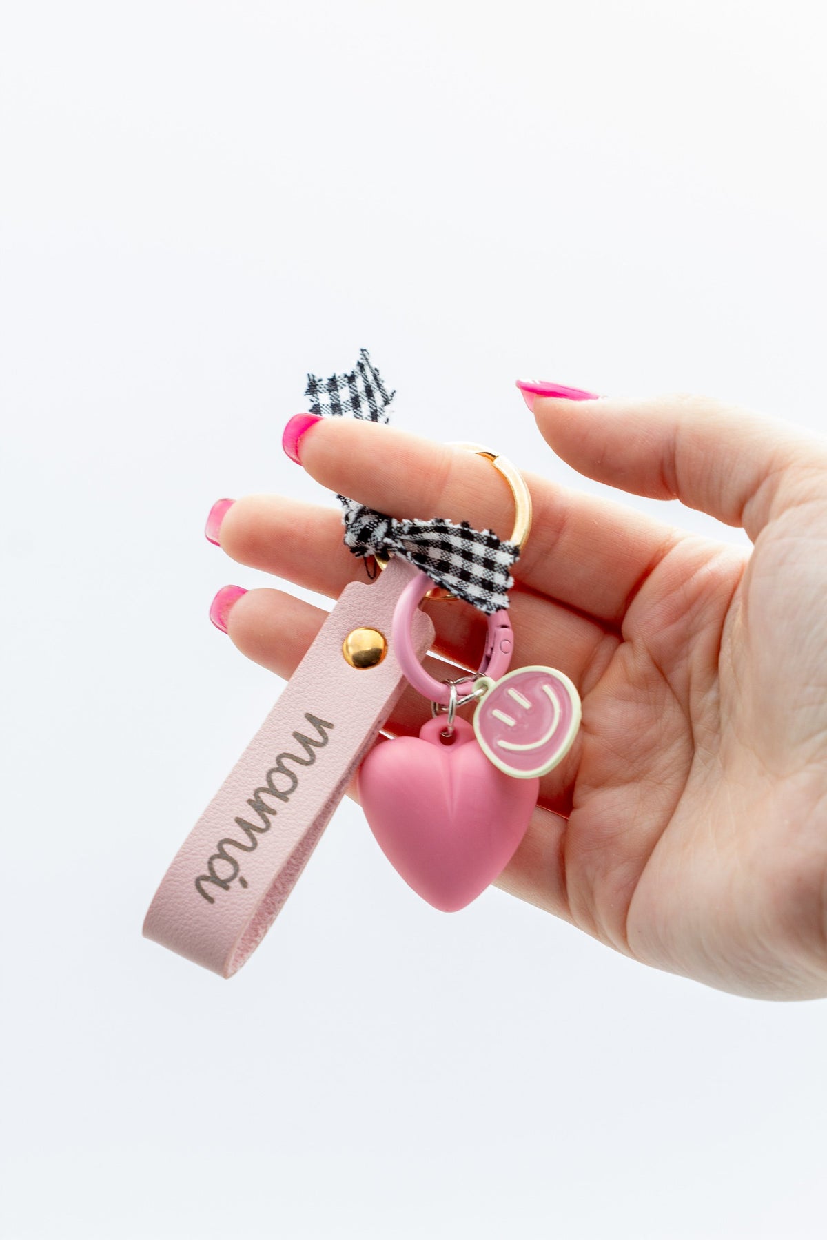 Mano sujetando llavero personalizado rosa con nombre grabado y colgante de corazón de silicona.