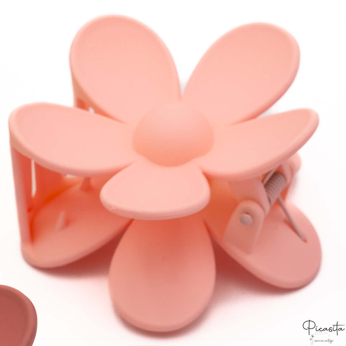 Pinza de pelo con forma de flor en color rosa claro melocotón con diseño de pétalos redondeados.