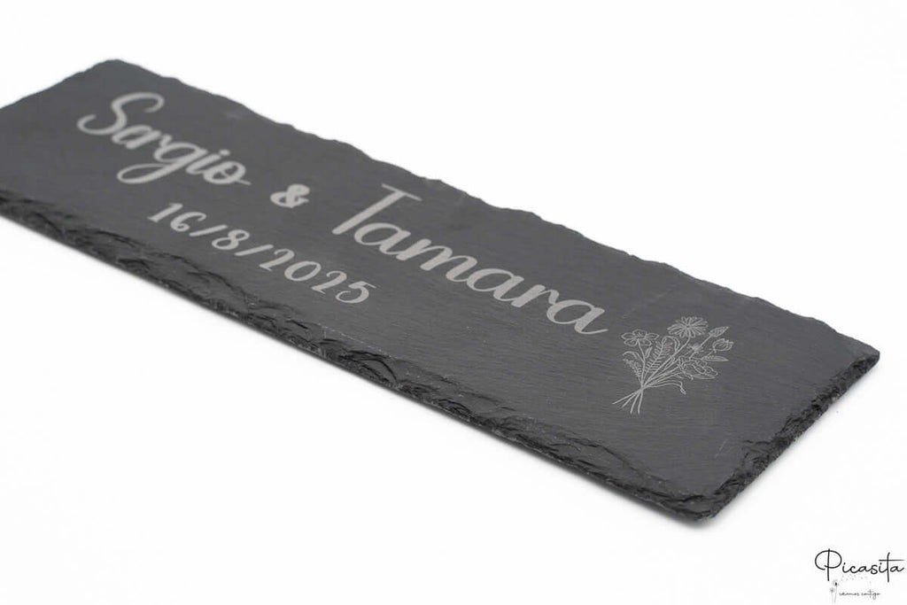 Vista lateral de plato de pizarra personalizado con diseño floral y nombres grabados a láser.